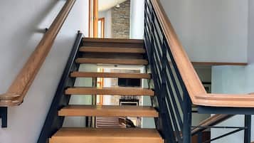 A staircase with wooden steps and black railings, leading to a room with a stone wall and a television.