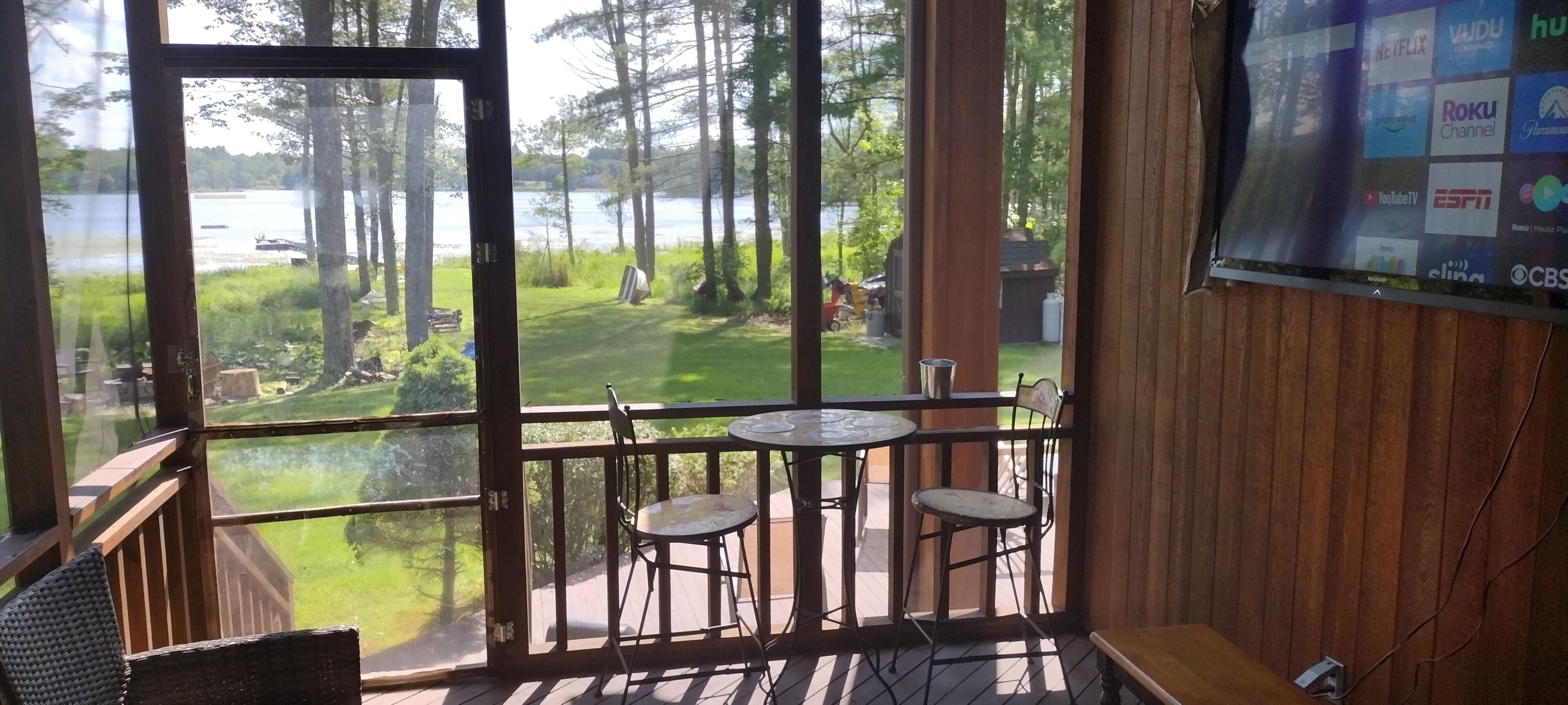 Una habitación con un ventanal grande con vistas a un área verde y una masa de agua. Hay dos sillas y una pequeña mesa en la habitación.