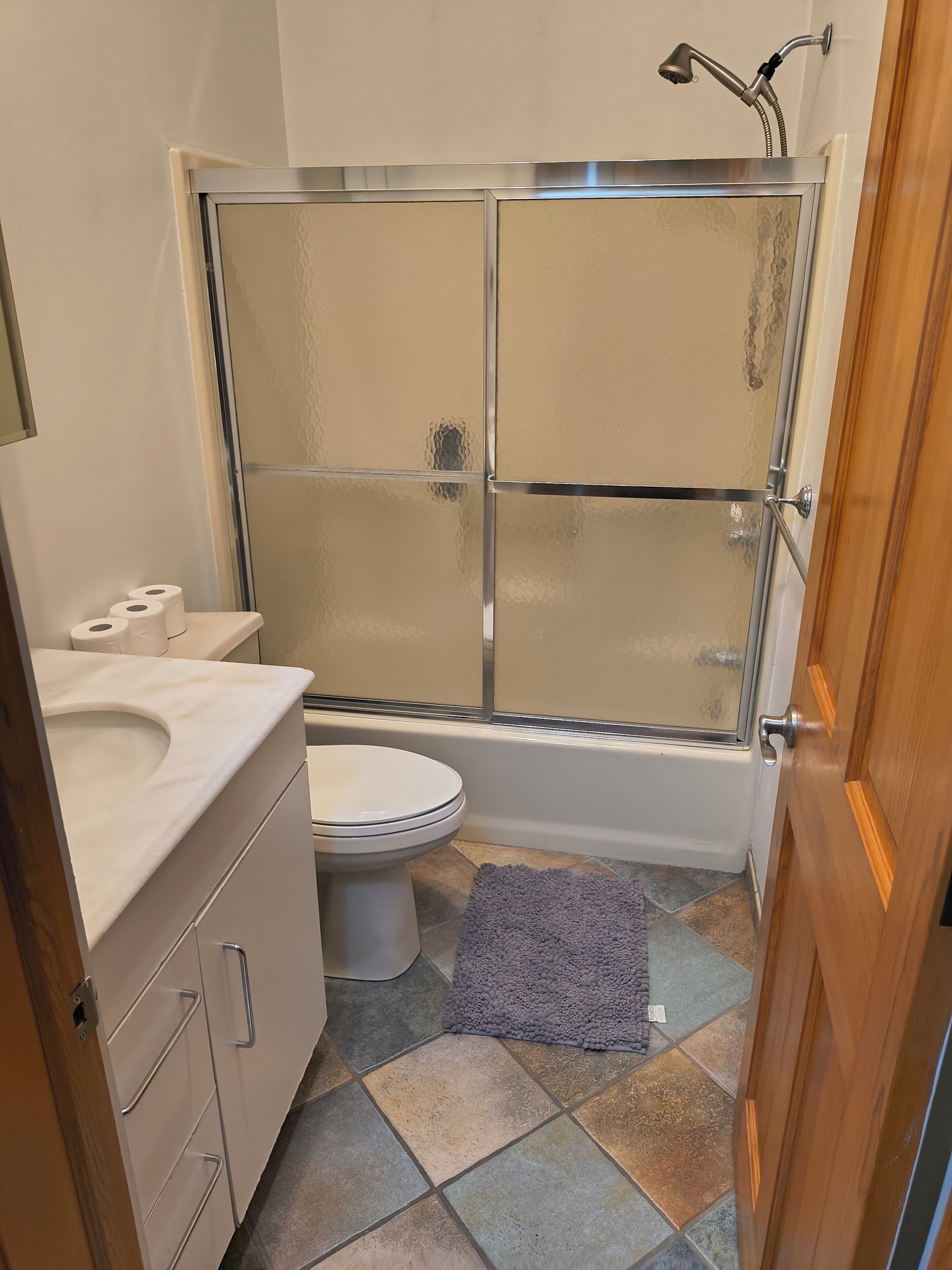 A bathroom with a glass-enclosed shower, a toilet, and a sink with a mirror.