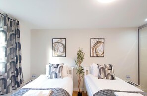 Quarto de hotel com duas camas, uma planta em vaso e arte abstrata na parede.