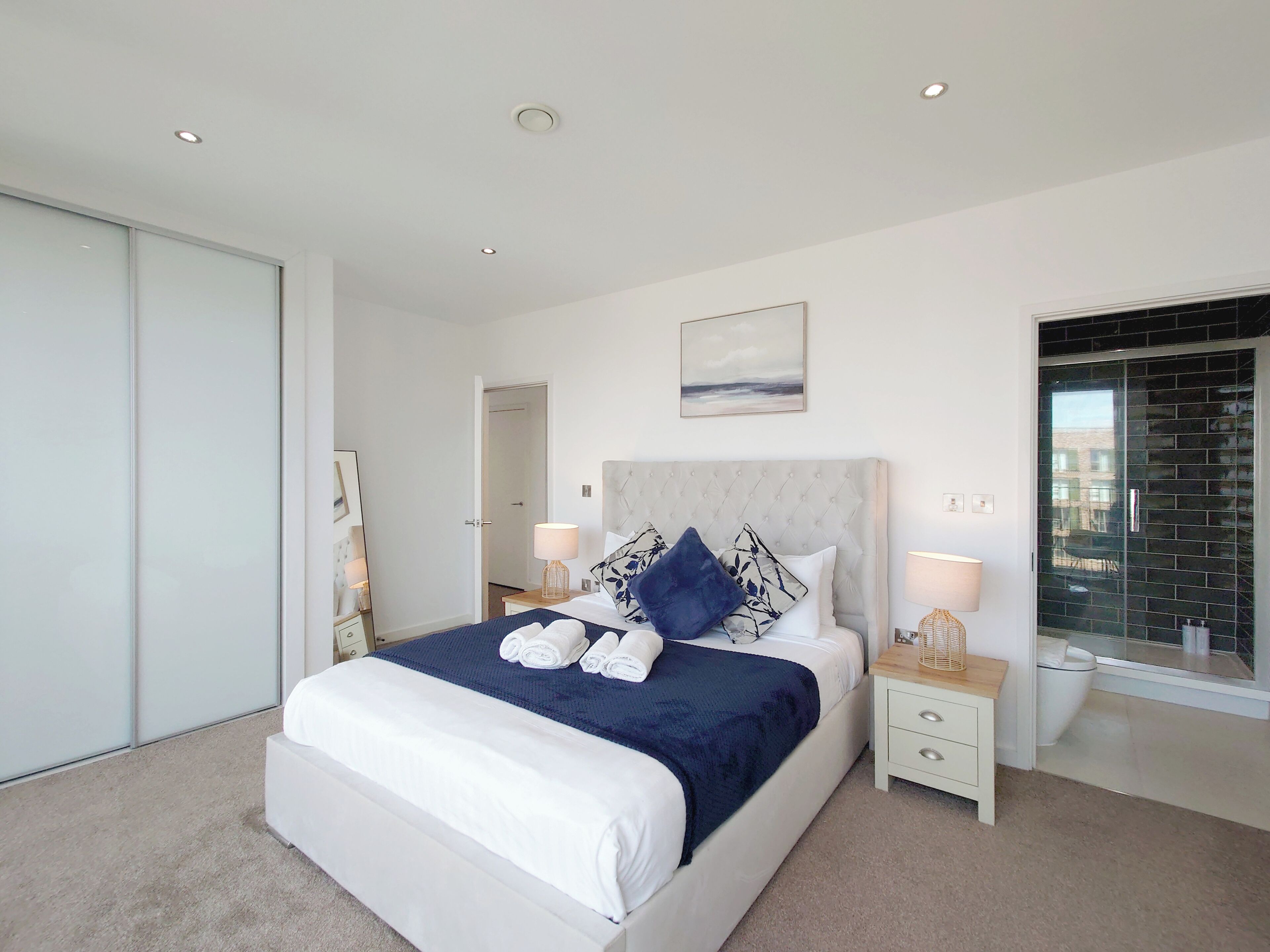 A modern bedroom with a large bed, bedside tables, a nightstand, a mirror, and a window with a view.