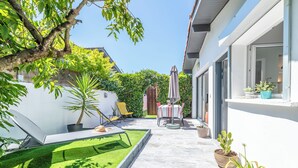 Een terras met een tafel en stoelen, omringd door potplanten en een kleintje gazon.