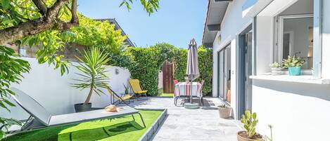 A patio with a table and chairs, surrounded by potted plants and a small lawn.