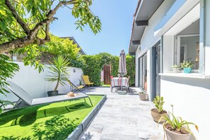 Eine Terrasse mit Tisch und Stühlen, umgeben von Kübelpflanzen und einem kleinen Rasen.