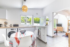 A modern kitchen with a dining area, large windows, and a view of greenery outside. - A 10-minute walk from the beach, a charming little house with a south-facing terrace (Anglet)