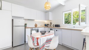Een moderne keuken met witte kasten, een eettafel met een kleurrijke tafelkleed en een hanglamp.