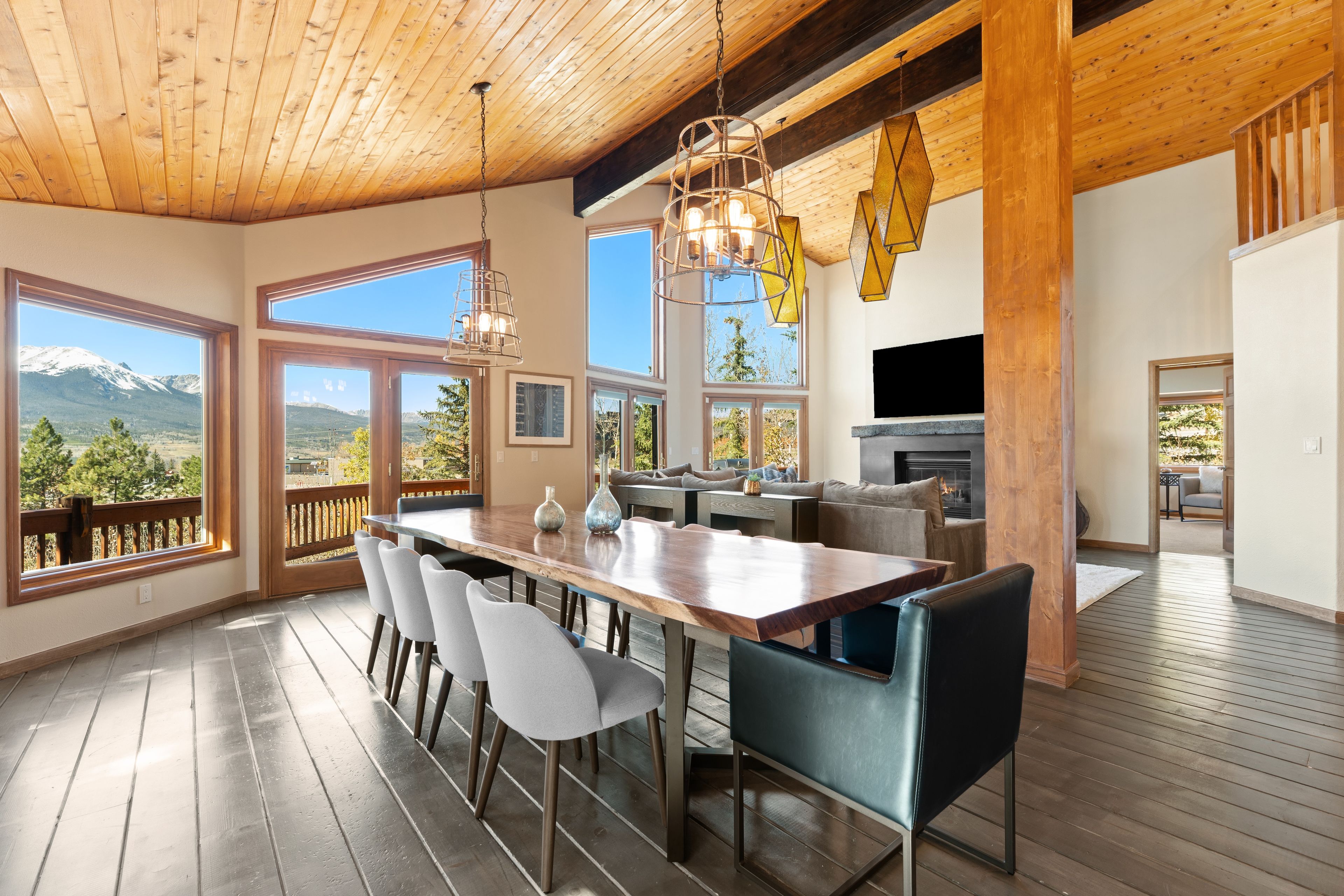 A spacious dining area with a wooden table and chairs, large windows with mountain views, and a fireplace.