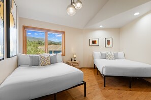 Ein Hotelzimmer mit zwei Betten, einem Fenster mit Bergblick und zwei gerahmten Kunstwerken an der Wand.