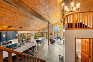 A spacious interior with a high ceiling, wooden beams, a kitchen area, dining space, and a view through large windows. - Spacious Mountain Home, Private Deck, Central Location in Dillon (Dillon)