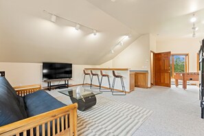 A living room with a sofa, a coffee table, a TV, and a bar area with stools. - Spacious Mountain Home, Private Deck, Central Location in Dillon (Dillon)
