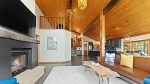 Een ruime woonkamer met een open haard, een houten plafond en uitzicht op de omgeving.