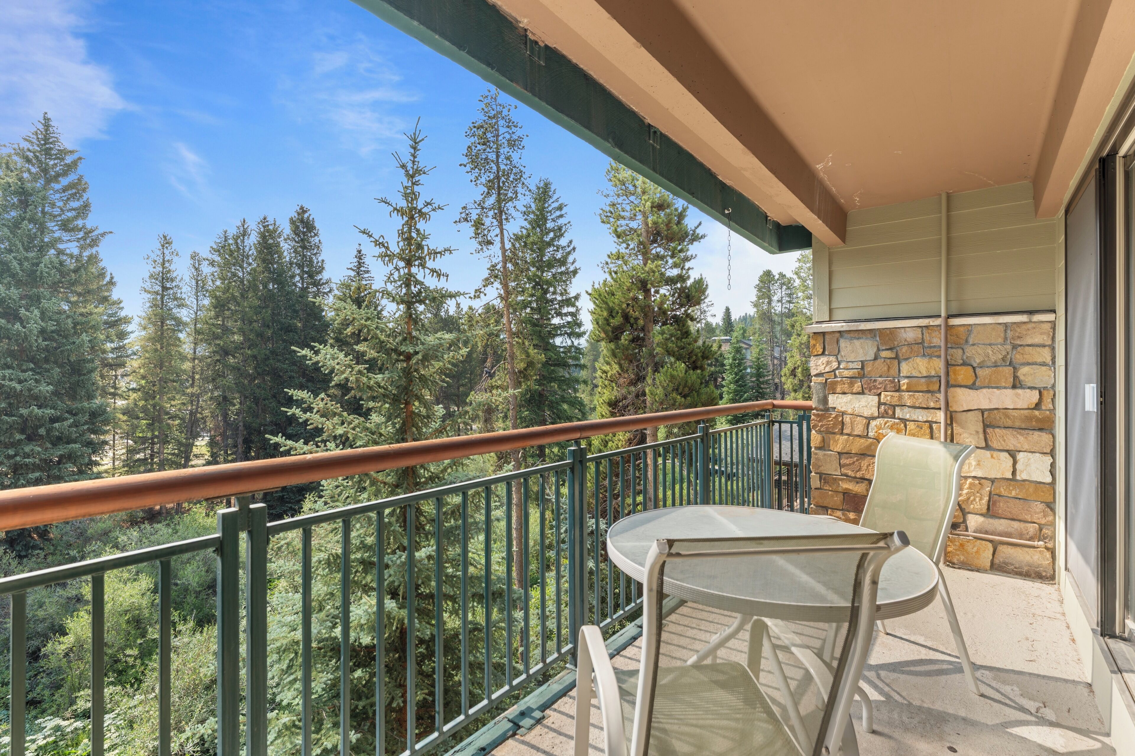A balcony with a table and chairs, overlooking a forested area.