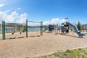 Un parque infantil con columpios, un tobogán y una estructura para escalar cerca de un lago.