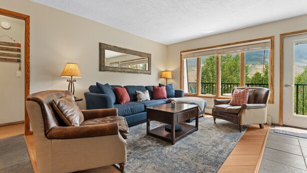 A spacious living room with a large sofa, a coffee table, and a leather armchair. There is a large window with a view of greenery. - Cozy Dillon Home: Skiing, Fishing, & Lakefront Living (Dillon)