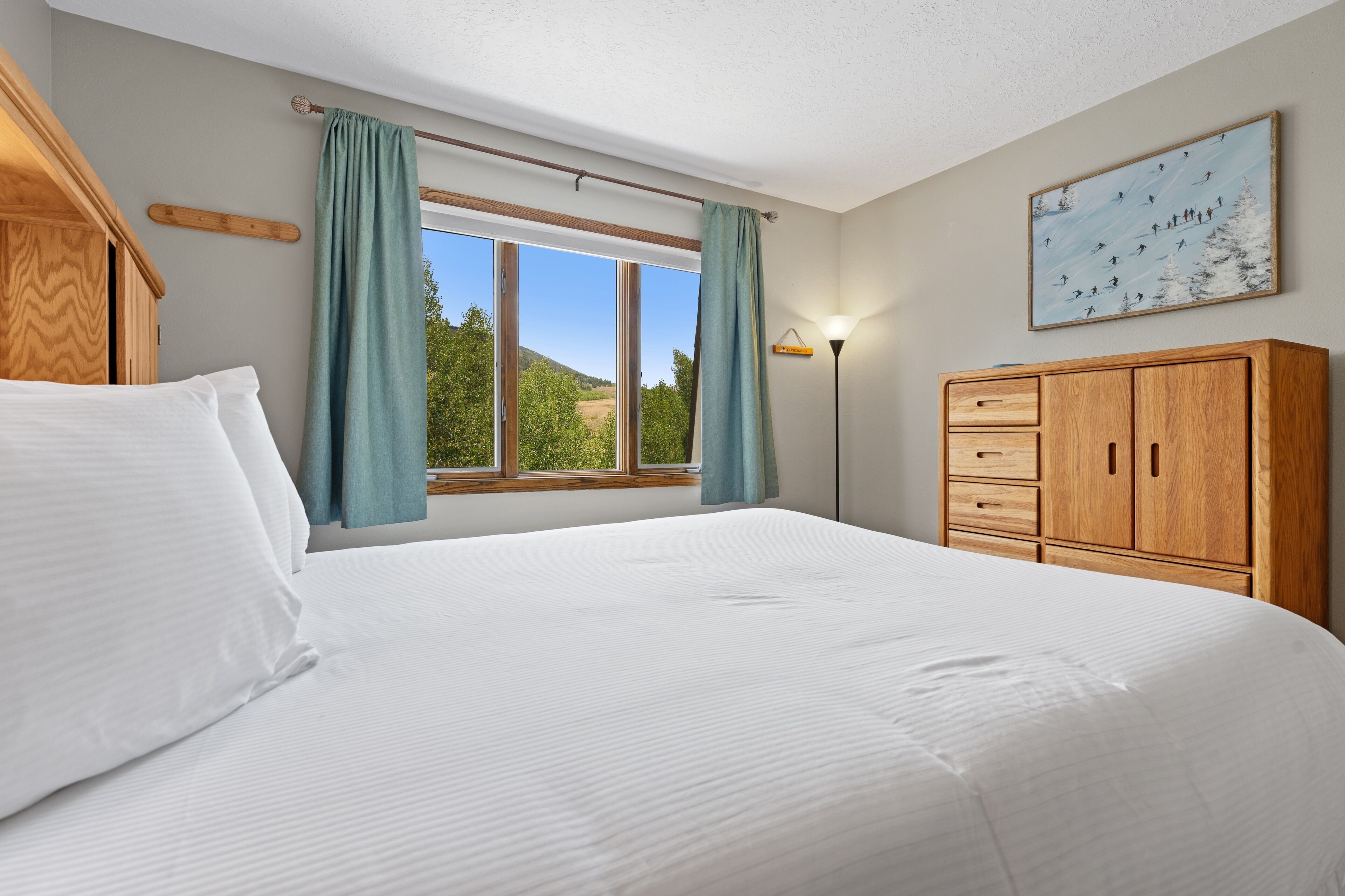 Un dormitorio con una cama grande, armario de madera, ventana con cortinas y un cuadro en la pared.