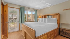 A bedroom with a wooden bed, a window with curtains, a door, and a small wooden dresser. - Cozy Dillon Home: Skiing, Fishing, & Lakefront Living (Dillon)