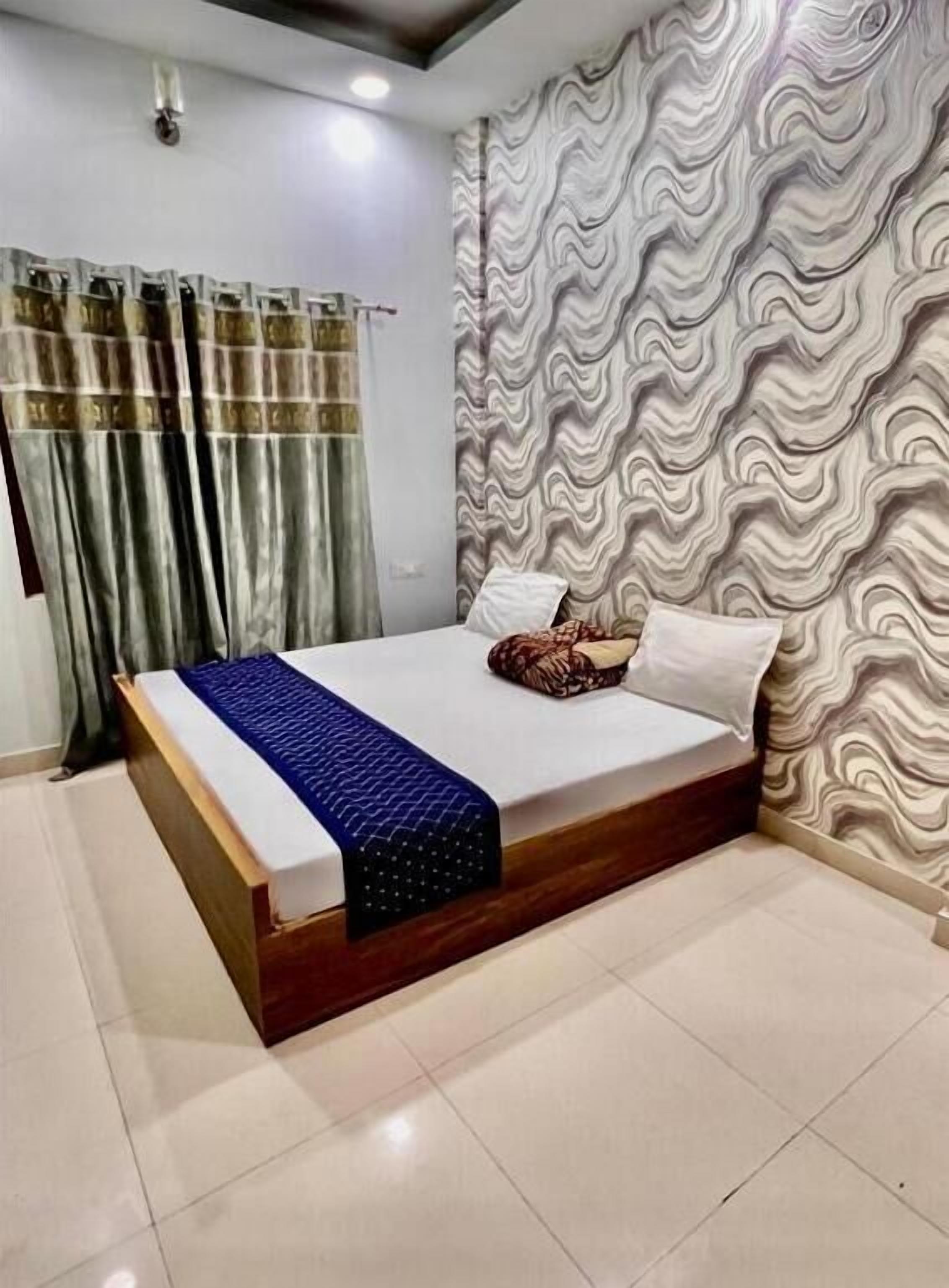 Un dormitorio con cama, cortinas y un papel tapiz estampado.