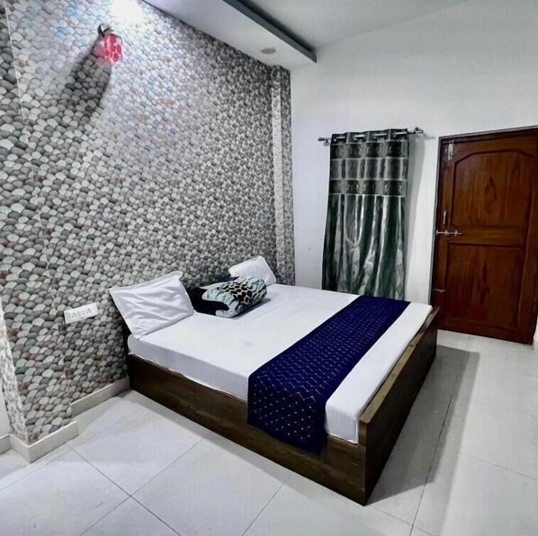 A bedroom with a bed, a wooden headboard, a stone wall, a wooden door, and a curtain. - THE GIRDHARI VARANASI (Varanasi)