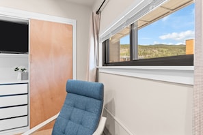 Une pièce dotée d’un placard avec une porte coulissante, d’une fenêtre donnant sur un paysage boisé et d’une chaise bleue.