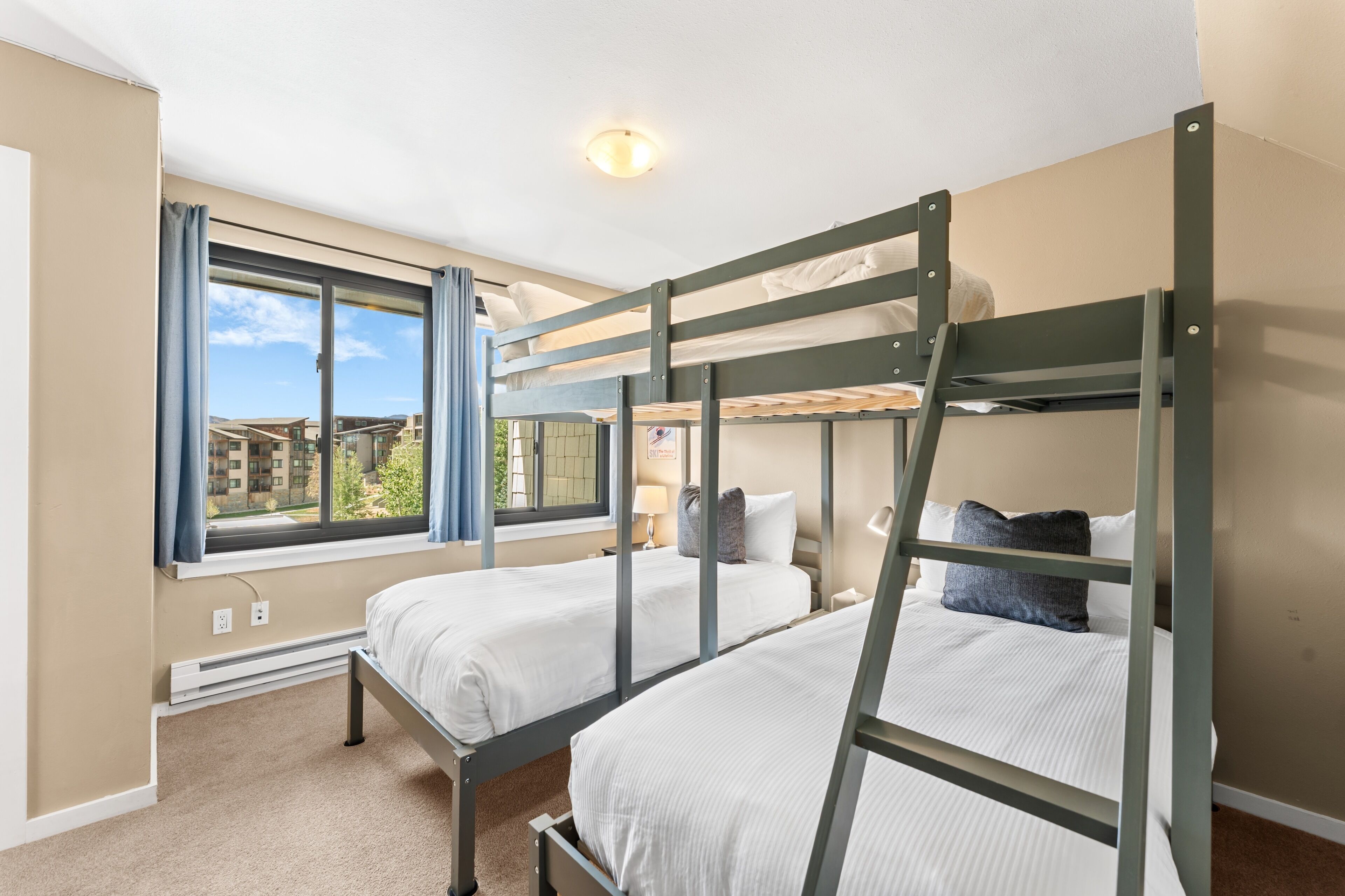 Habitación con dos literas, ventana con cortinas, una lámpara en el techo y vistas a edificios.