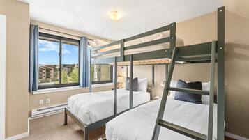 Habitación con dos literas, ventana con cortinas, una lámpara en el techo y vistas a edificios.