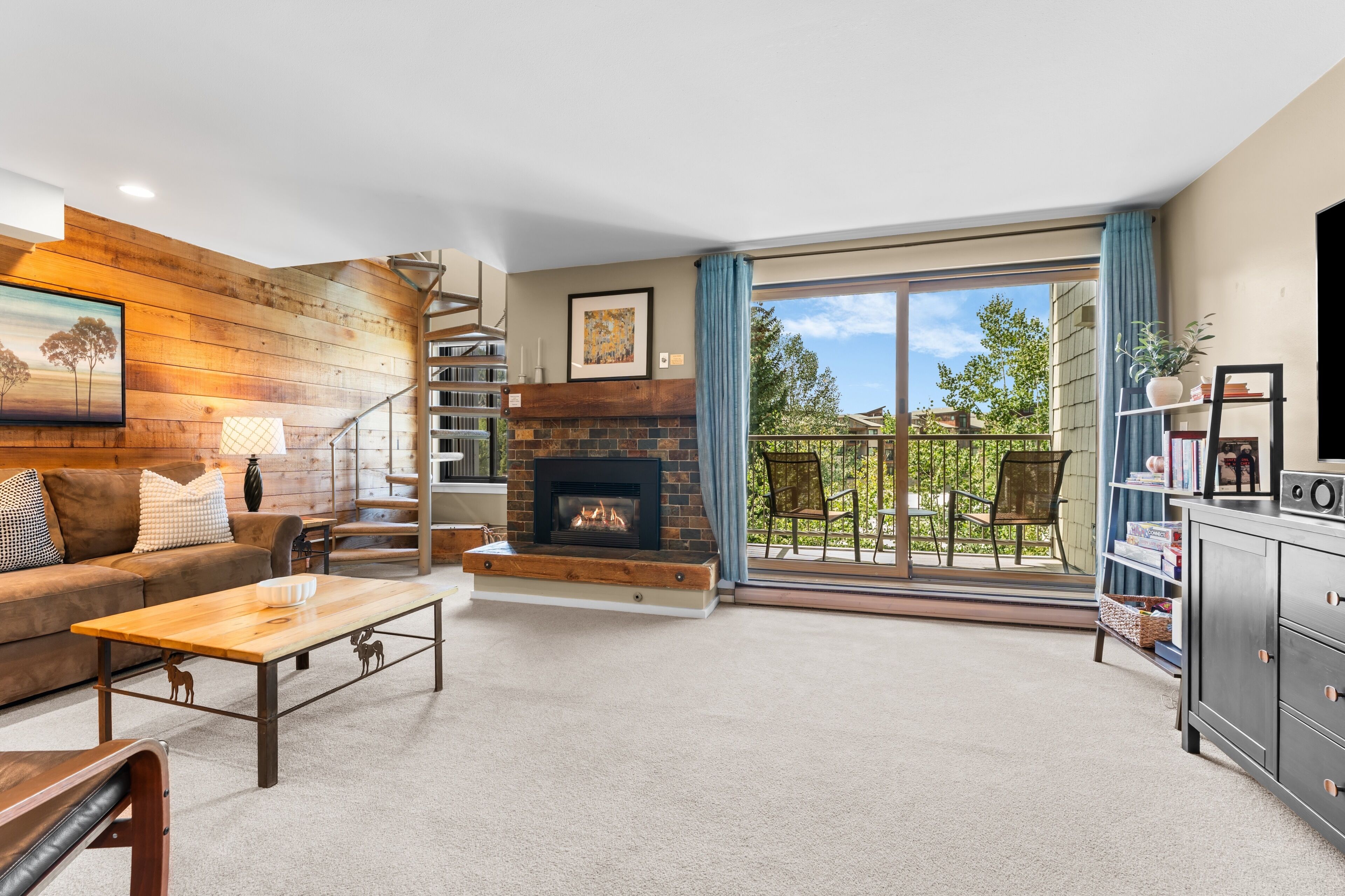 A living room with a fireplace, a staircase, a sofa, a coffee table, and a view of the outdoors.