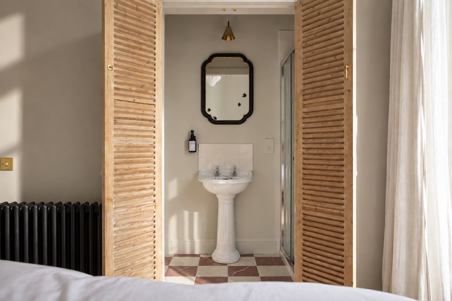 A hotel bathroom with a checkered floor, a pedestal sink, a mirror, and a radiator.