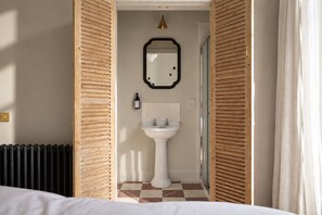 A hotel bathroom with a checkered floor, a pedestal sink, a mirror, and a radiator. - Manna House | The Grand (East Lothian)