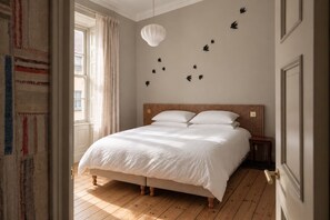 A bedroom with a large bed, wooden headboard, and a wall-mounted light fixture.