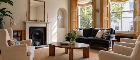 Una sala de estar con chimenea, un sofá negro, una mesa de centro redonda y una estantería.