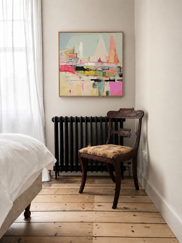 A bedroom with a bed, a chair, a radiator, and a painting on the wall.