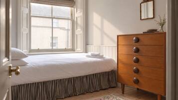 A bedroom with a bed, a dresser, a window with blinds, a mirror, and a patterned rug.