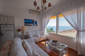 Une pièce comprenant un canapé, une petite table, une lampe, un tableau et une vue sur la mer.