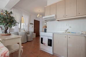 Une cuisine compacte avec un îlot central, un coin repas avec des chaises en osier et une plante en pot.
