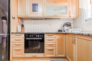 A kitchen with wooden cabinets, a built-in oven, a coffee maker, and a sign with family rules. - Tilias House by Rentals Pro - Nea Flogita Halkidiki (Nea Flogita)