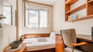 Ein kleines Hotelzimmer mit Bett, Schreibtisch, Stuhl, Nachttisch mit einer Schale und einem Fenster.
