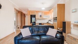Ein modernes Wohnzimmer mit einer schwarzen Ledersofa, Holzschränken und einer Küche im Hintergrund.