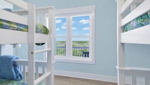 Una habitación con literas, una ventana con vistas a follaje y una pared azul claro.
