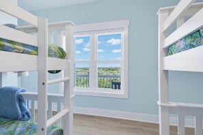 Ein Zimmer mit Etagenbetten, einem Fenster mit Blick auf Grünflächen und einer hellblauen Wand.