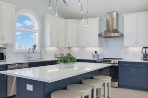 A modern kitchen with white cabinets, a stainless steel range hood, and a central island with stools. - Oceanfront pool, hot tub and game room (North Topsail Beach)