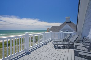 Eine Holzterrasse mit weißen Geländern, die auf einen Strand und den Ozean blickt.