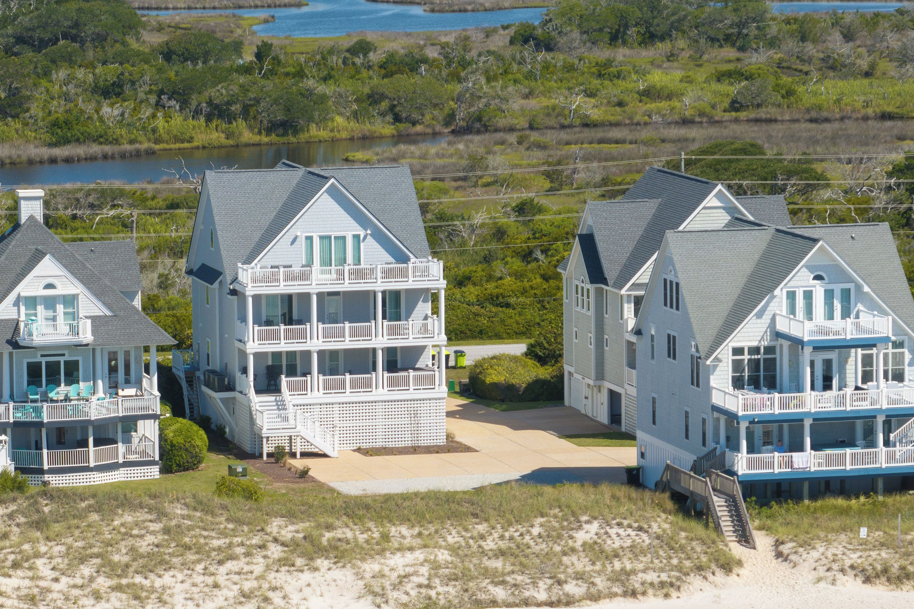 A beachfront property with multiple-story houses featuring balconies, a sandy beach in the foreground, and a body of water in the background.