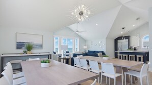 Una cocina moderna con una isla central, un comedor con sillas blancas y un amplio ventanal con vistas al mar.