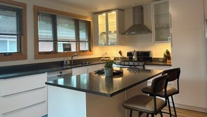 A modern kitchen with a central island, built-in appliances, and a window with blinds. - Sharp Mid-Century Modern Home with Hot Tub -- Old North Boulder (Boulder)