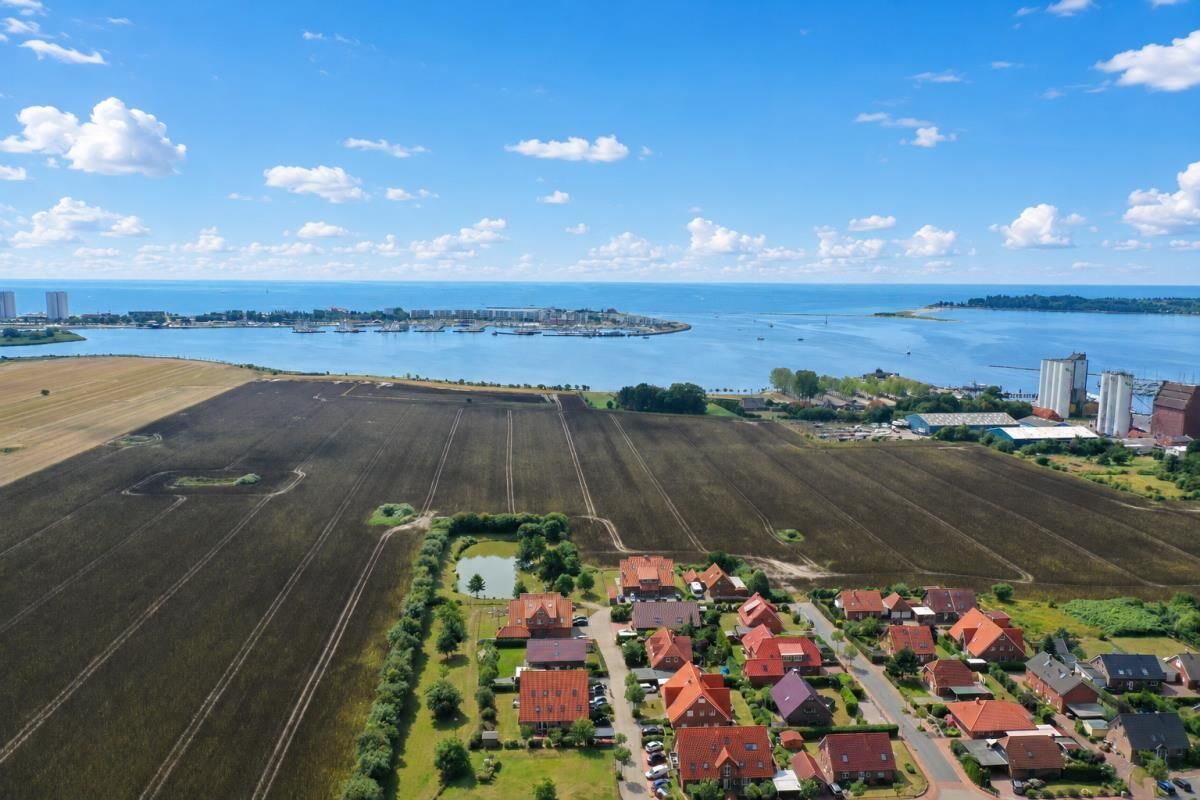 An aerial view of a coastal residential area with houses, fields, and a marina.