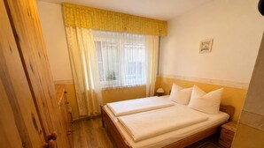 Ein Doppelbett mit weißer Bettwäsche, ein Holzschrank, ein Nachttisch und ein Fenster mit transparenten Vorhängen.