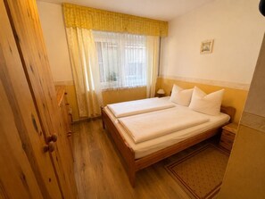 A double bed with white linens, a wooden wardrobe, a bedside table, and a window with sheer curtains. - 10 Vacation Rental "Anders Fewo 1" (Burg auf Fehmarn)