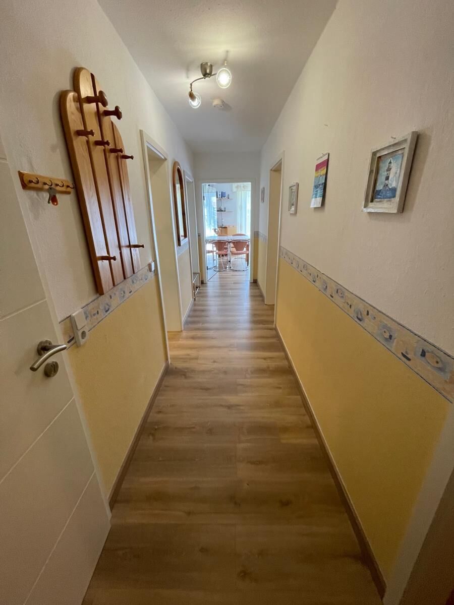 A hallway with wooden flooring, white walls, and a ceiling light fixture.