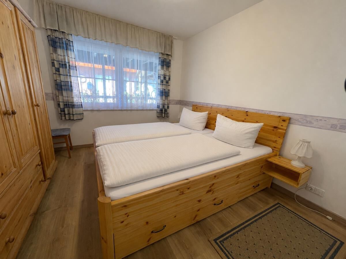 A bedroom with a wooden bed, a nightstand, a bench, and a wardrobe.