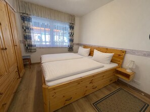 A bedroom with a wooden bed, a nightstand, a bench, and a wardrobe. - 10 Vacation Rental "Anders Fewo 1" (Burg auf Fehmarn)